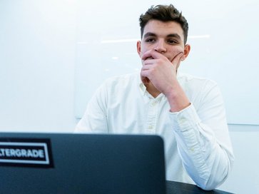 Ein junger Mann der vor einem Laptop sitzt und nachdenkt